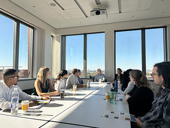 A group of people sit around a table in a sunny conference room.